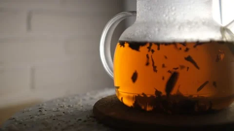 Close-up of brewing black tea in a glass teapot. The tea leaves play in the ligh Stock Footage 148386066