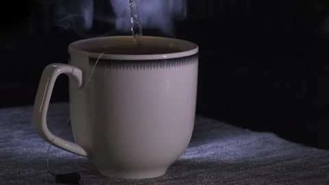 Close-up of brewing tea in a tea bag in a white cup. Dark background, steam Stock Footage 302438409