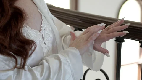 A close-up of a bride in a luxurious white robe admiring her diamond engagement Stock Footage 322840766