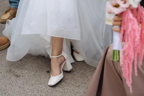 Close up of a bride walking in elegant white block heel shoes holding up her Stock Photos