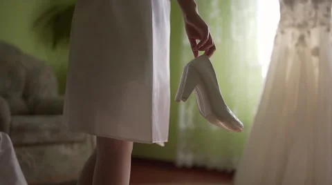 Close-up of a bride with wedding shoes in hes hands. At the bottom of it says Stock Footage