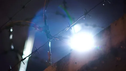 Close-up of bright light shining through barbed wire at night. Footage. Close-up 動画素材 129093378