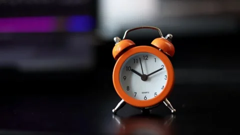 Close-up of a bright orange twin bell alarm clock on a reflective surface Stock Footage 337104463