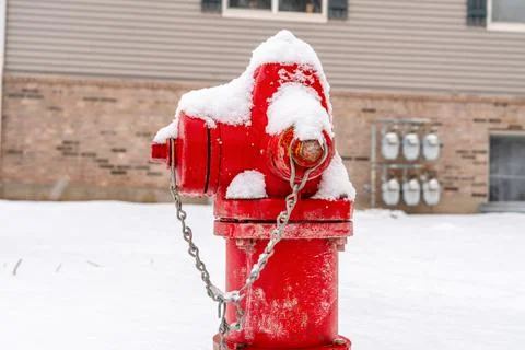Close up of a bright red fire hydrant against snow and building in winter Stock Photos