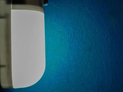 Close up of bright white LED wall lamp glowing against textured blue wall Stock Photos