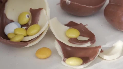 Close-Up of Broken Chocolate Egg Shells with Colorful Easter Candy Inside Stock Footage 332944056