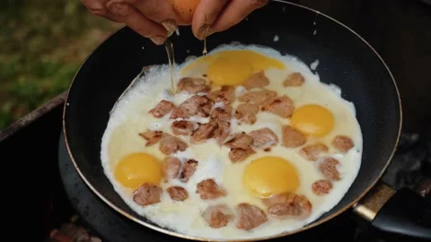 Close-up of broken egg falls into the frying pan. Eggs and bacon, green grass on Video stock 205848500