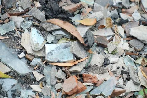 Close-up of broken glass, ceramic shards, and rubble mixed with dry leaves. 스톡 사진