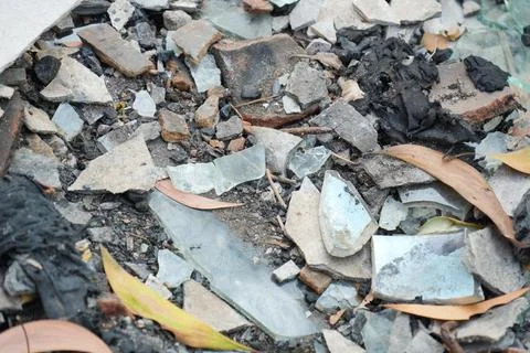 Close-up of broken glass, ceramic shards, and rubble mixed with dry leaves. Stock-Fotos