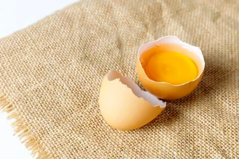 Close up broken raw egg with the yolk and albumen on a linen tablecloth on wh Stock Photos