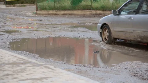 Close-up broken road with dirty puddles on which cars passing with difficulty Stock Footage 101540221