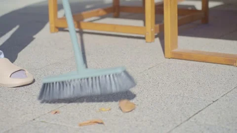 Close up of broom sweeping dry fallen leaves from patio tiles. Patio cleaning Stock Footage 348173922
