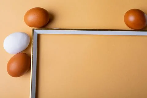 Close-up of brown and white easter eggs around empty frame on orange background 库存照片