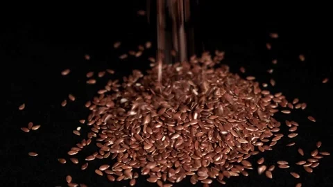 Close-up of brown flax seeds being poured into a pile on a black background, emp Stock Footage 295225334