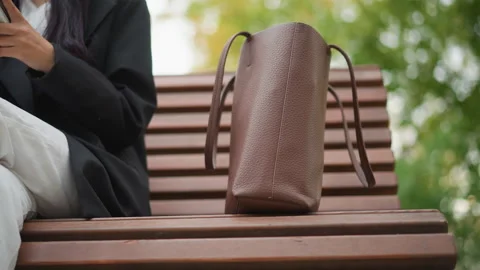 Close up of brown leather handbag placed on wooden bench with person in dark Stock Footage 346649384