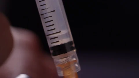 Close-up of brown liquid heroin getting sucked up into a syringe from a needle Stock Footage
