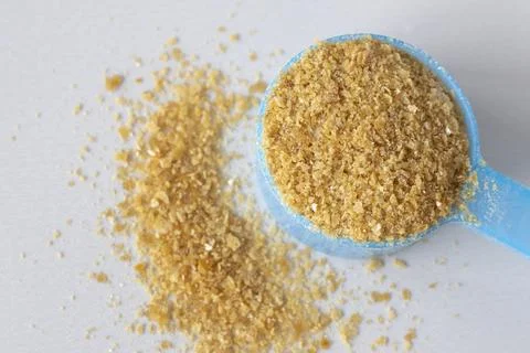 Close-up of brown pellets of bone broth in a blue spoon against a beige Stock Photos