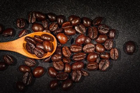 Close-up of brown, roasted coffee beans in a wood spoon background. Stock Photos