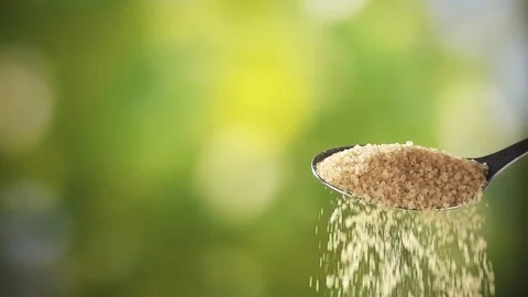 Close up of brown sugar pouring from spoon on natural green background Stock Footage