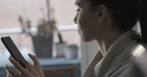 Close up browsing and texting on her phone by the window - 4K Stock Footage 96318665