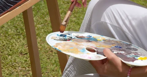 Close-up of a brush in a woman's hands picking up acrylic paint on a palette for Stock Footage 234950844