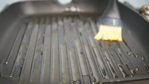 Close-up brushing with a silicone brush a grilling pan with olive oil in 4K. Stock Footage 154434370