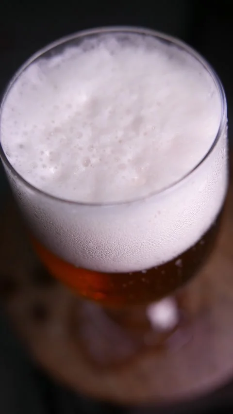 Close-up of bubbles popping in beer foam head. A glass of beer on the table. Stock Footage 333656314