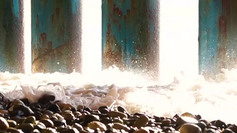 Close-up, bubbling foam wave beats out of light through rusty columns Stock Footage 169810343