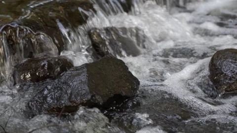 Close-up bubbling water flowing over river stones 스톡 동영상 323772531