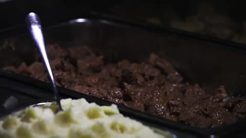 Close up buffet trays with spoon in mashed potatoes and cooked meat indoors Stock Footage 335473568