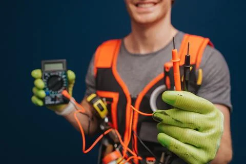 Close up builder is holding digital multimetert in gloves, isolated over blue Stock Photos