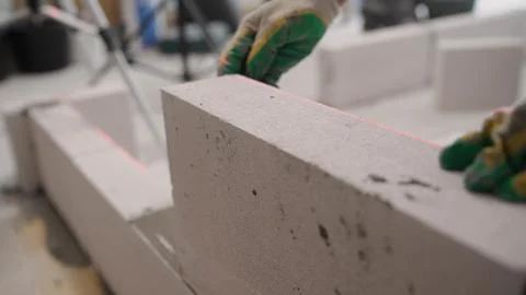 Close-up of a builder laying a grey concrete block, guided by a red laser lev Stock Photos
