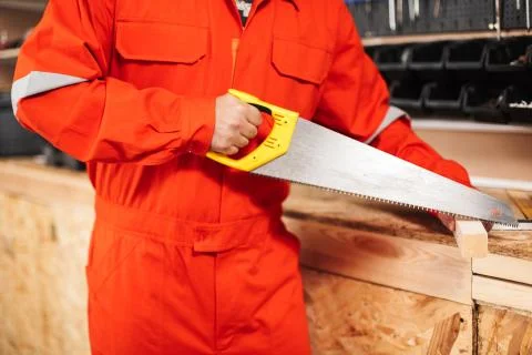 Close up builder in orange work clothes sawing wooden plank with Foto stock