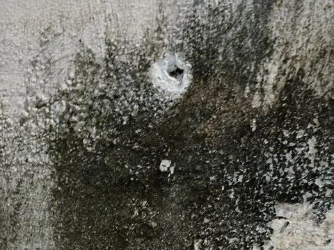 Close-up of a bullet hole or damage on a weathered concrete wall. Stock Photos