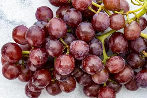 A close up of a bunch of juicy red grapes with stems on a white marble Stock Photos