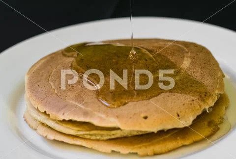 Close up of a bunch of tasty american pancakes and maple syrup poured over th Stock Photos