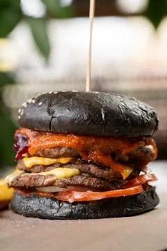 Close-up of burger with black bun with beef and bacon on table with cheese .. Stock Photos