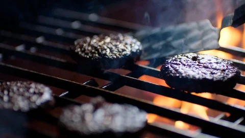 Close up of burger chops on grill with fire flames, chef turns them over, slow Video stock 92693984
