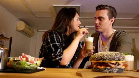 Close up burgers in defocus and woman and man tasting coffee in focus Stock Footage