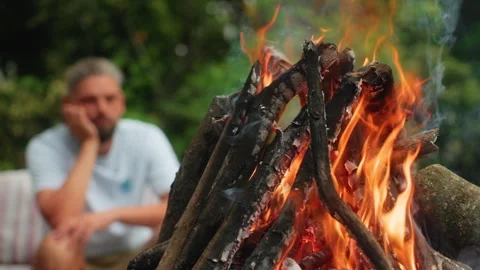 Close-up of burning campfire with thoughtful man sitting in blurred background. Stock Footage 338366564