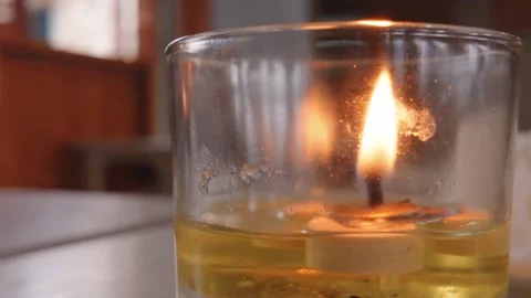 Close up of a burning candle inside a glass jar filled with yellow oil. Video stock 343402637