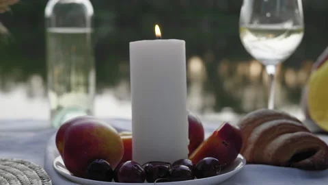 Close-up, Burning Candle Stands Among Fruits at Evening Picnic on riverside Stock Footage 145943890