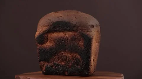 Close up of burnt loaf of rye bread rotates on wooden board on brown background. Stock Footage 243735601