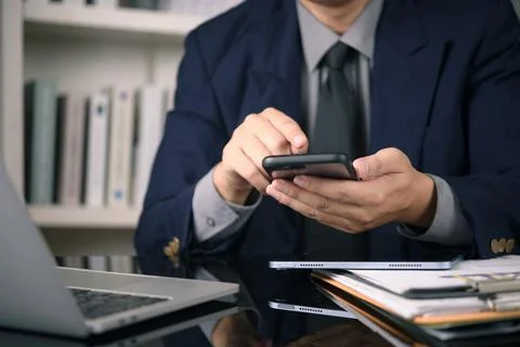 Close up businessman hands using smartphone typing message office desk lapt.. 스톡 사진