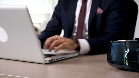 Close up businessman types on computer than picks up a VR headset Stock Footage 95231099