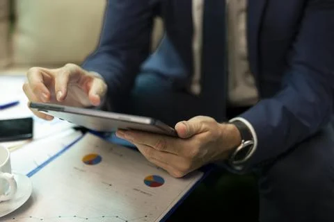 Close up of businessman using tablet above printed charts and reports 스톡 사진