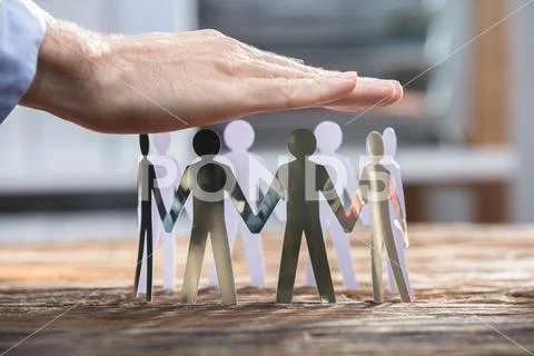 Close-up Of A Businessperson Protecting Human Cut-out Figures Stock Photos