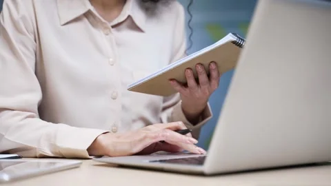 Close up of businesswoman's hands taking notes in notebook while using laptop Stock Footage 297276721