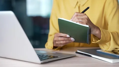 Close-up of businesswoman’s hands writing notes in notebook while using laptop  Stock Footage 328219846