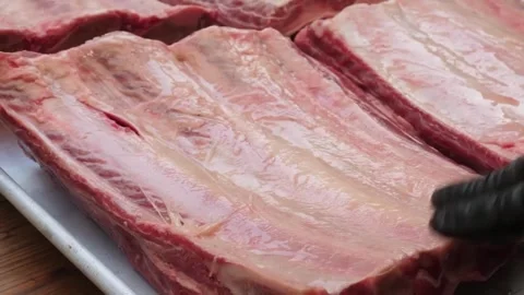 Close-up of a butcher or chef's hand in a black glove inspecting a large raw rac Stock Footage 338212343